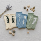 three pairs of socks with motivational phrases on a textured surface with decorative elements.
