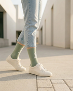Person wearing light green socks with white sneakers and jeans on a paved surface.