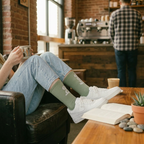 Person sitting on a couch holding a coffee cup in a cozy cafe setting.