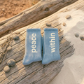 Two blue socks with 'peace within' text on a wooden surface with pebbles.